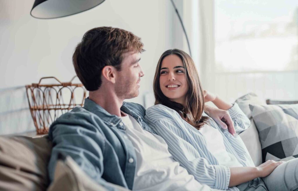 A couple sitting together, smiling warmly at each other, showing healthy habits for couples.
